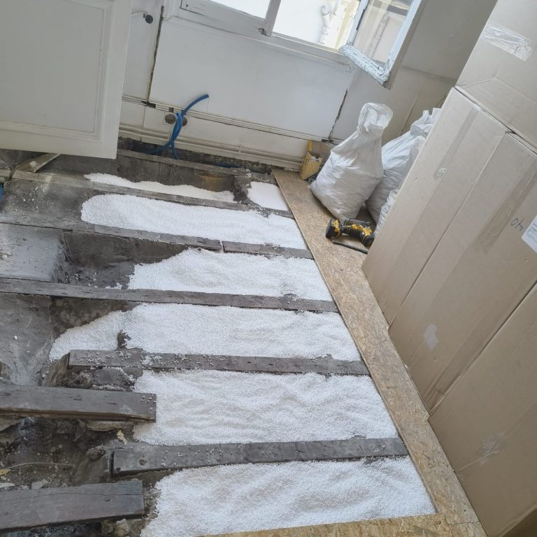 Sol en cours de rénovation, avec des poutres et de la poudre sur le sol.